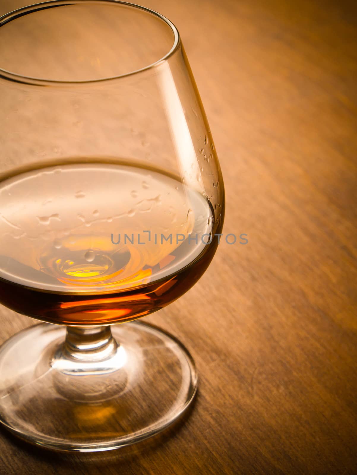 One glass of cognac on a wooden table