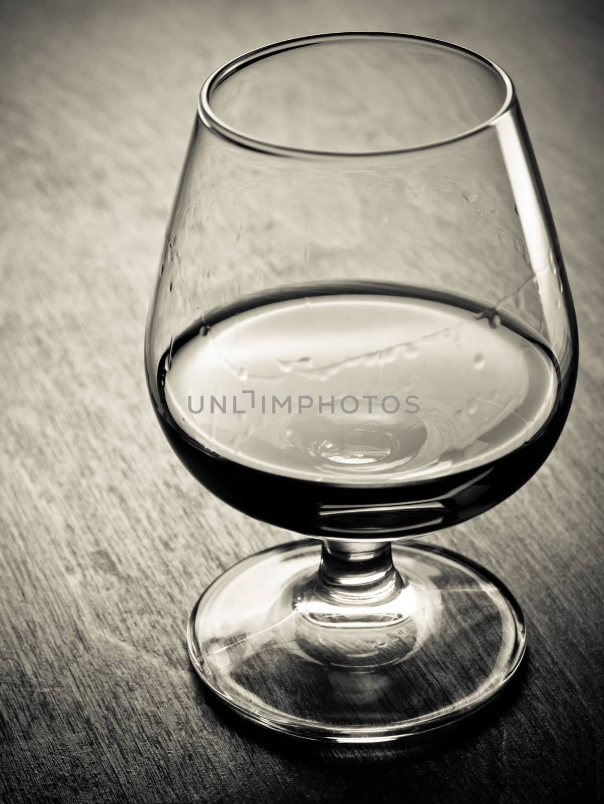 One glass of cognac on a wooden table