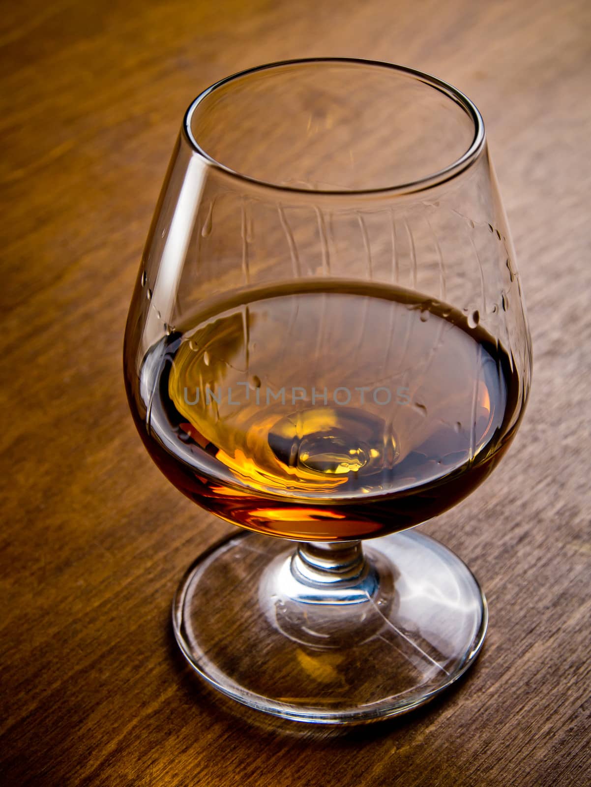 One glass of cognac on a wooden table