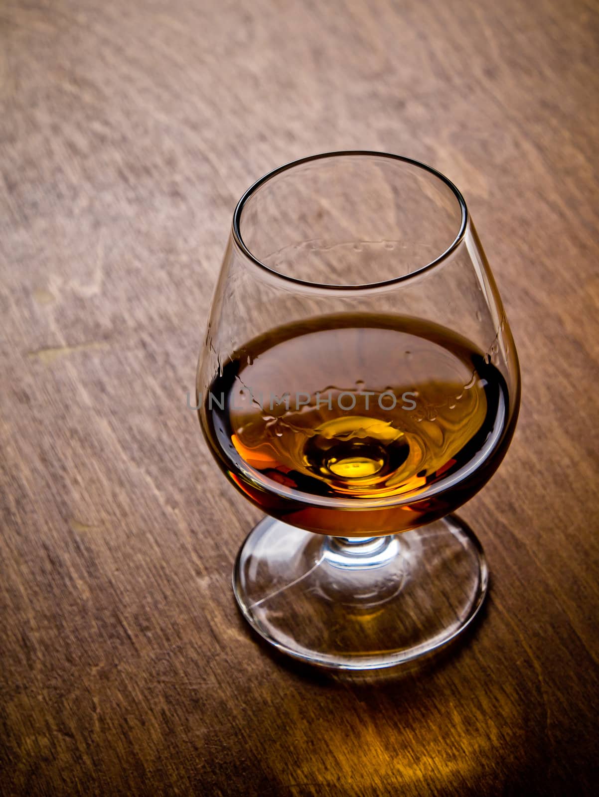 One glass of cognac on a wooden table