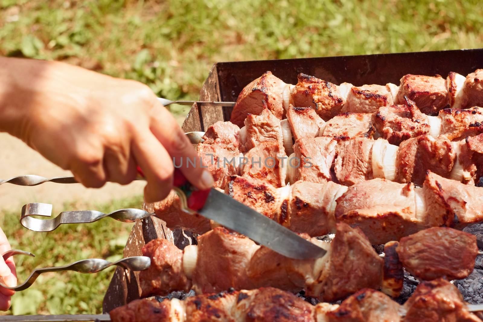 Preparation of meat slices on the metal skewers close up outdoors in summer