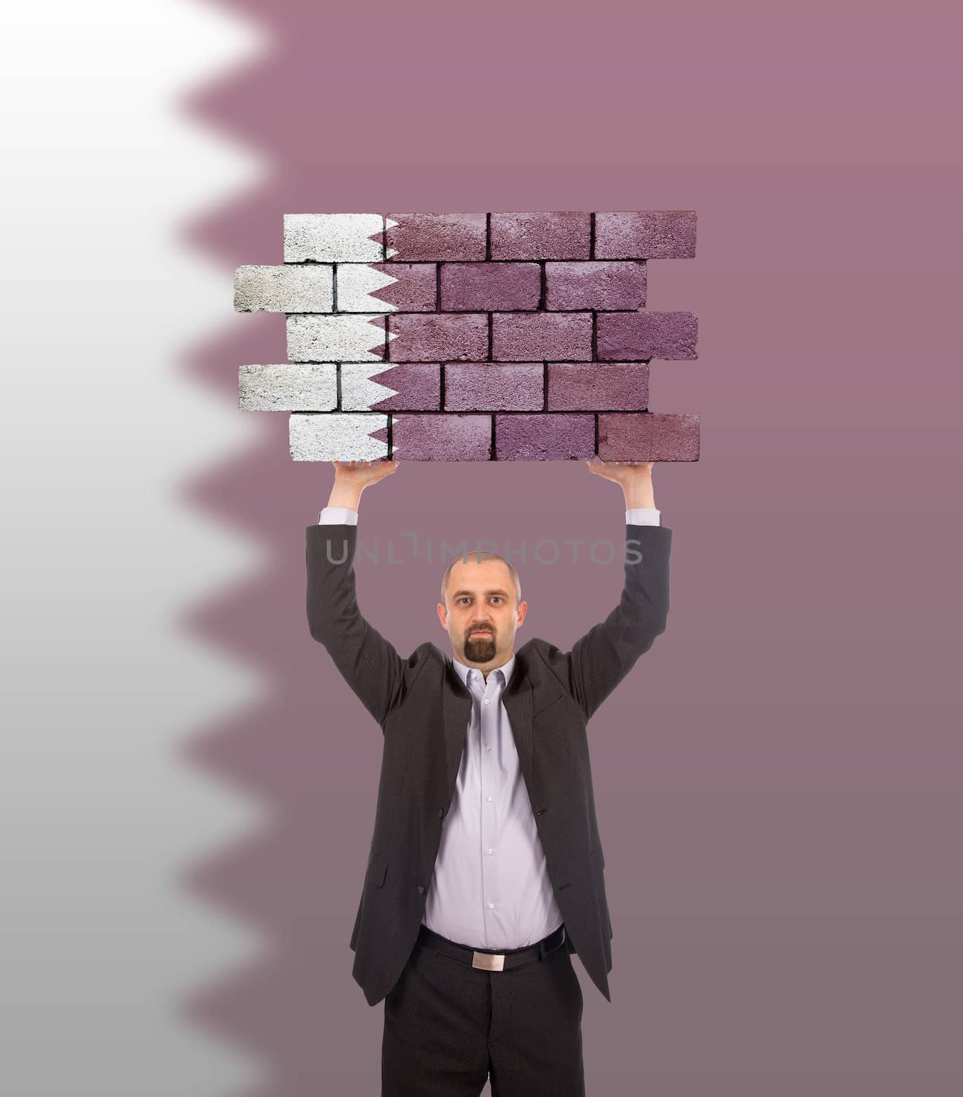 Businessman holding a large piece of a brick wall, flag of Qatar, isolated on national flag