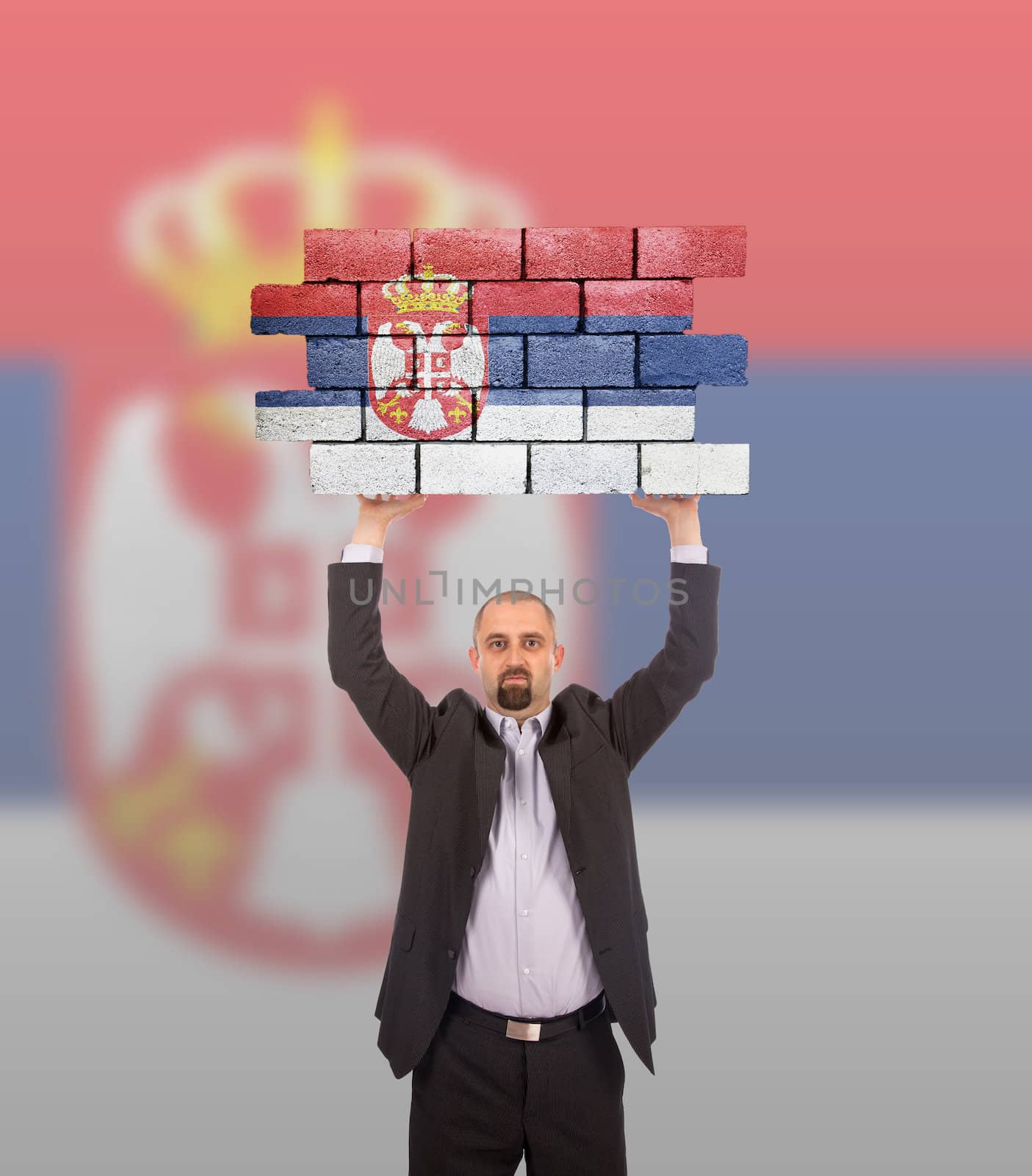 Businessman holding a large piece of a brick wall, flag of Serbia, isolated on national flag