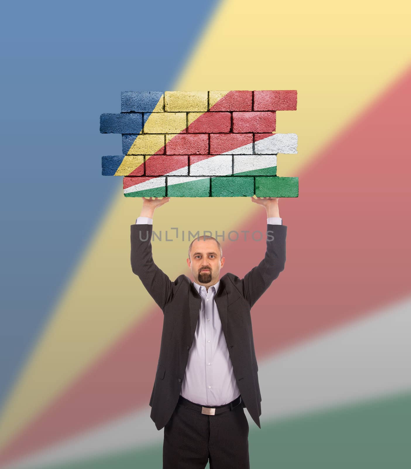 Businessman holding a large piece of a brick wall, flag of the Seychelles, isolated on national flag
