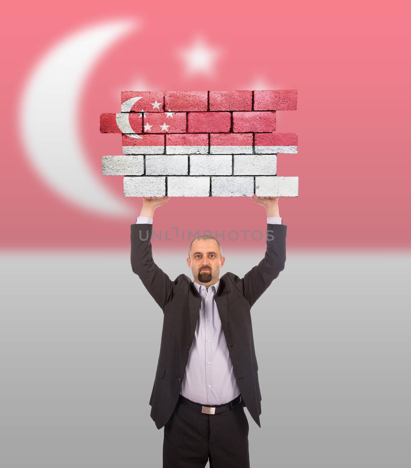 Businessman holding a large piece of a brick wall, flag of Singapore, isolated on national flag