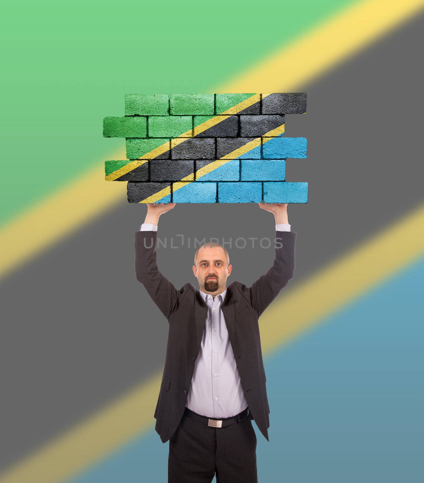 Businessman holding a large piece of a brick wall, flag of Tanzania, isolated on national flag