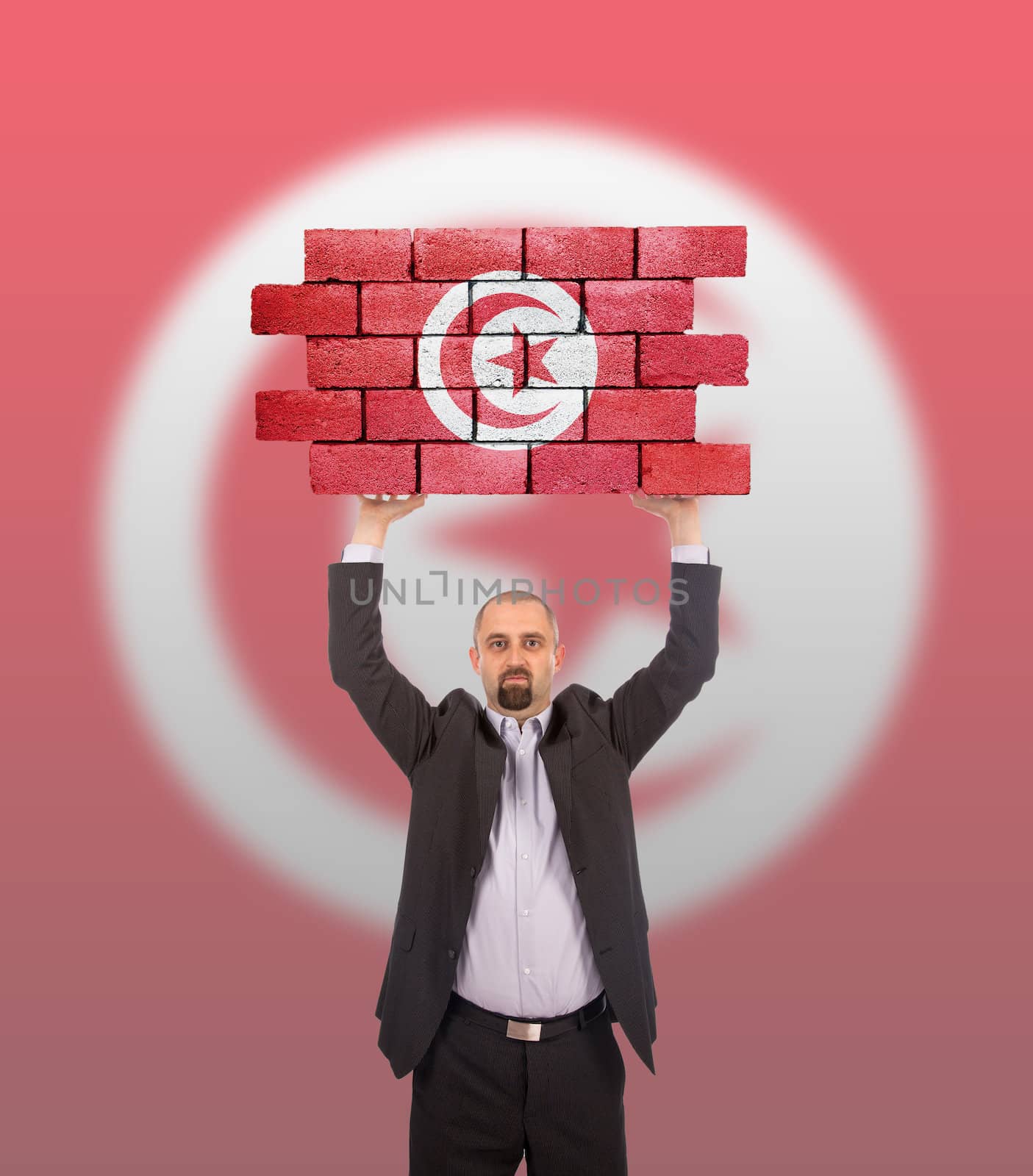 Businessman holding a large piece of a brick wall, flag of Tunesia, isolated on national flag
