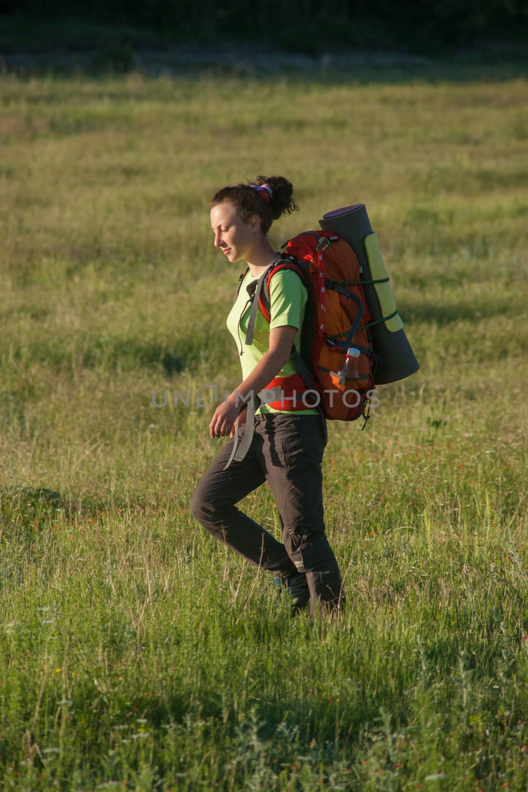 Happy smiling woman in field. Green grass in foreground and clear sky in background.