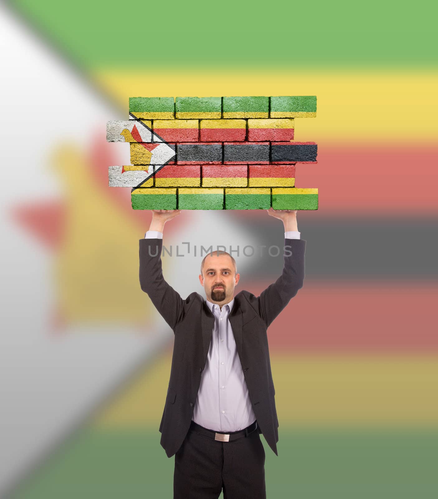 Businessman holding a large piece of a brick wall, flag of Zimbabwe, isolated on national flag