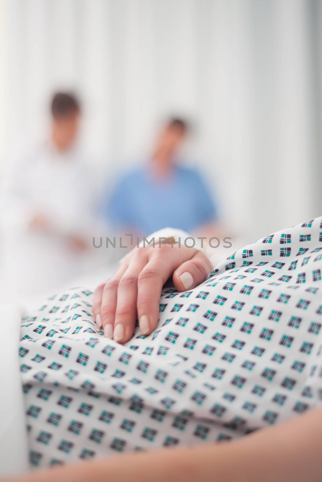 Closeup on the hand of a lying patient in a hospital with her family in background