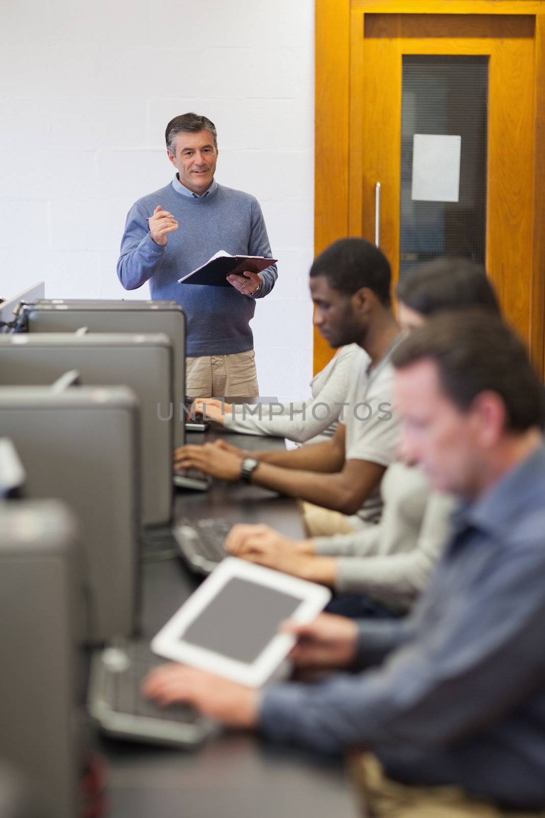 Teacher talking to his computer class holding a clipboard in college