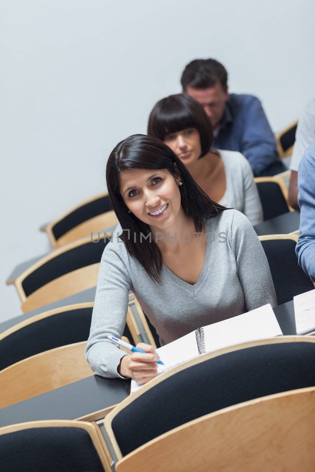 Smiling woman looking up from note taking during lecture in college