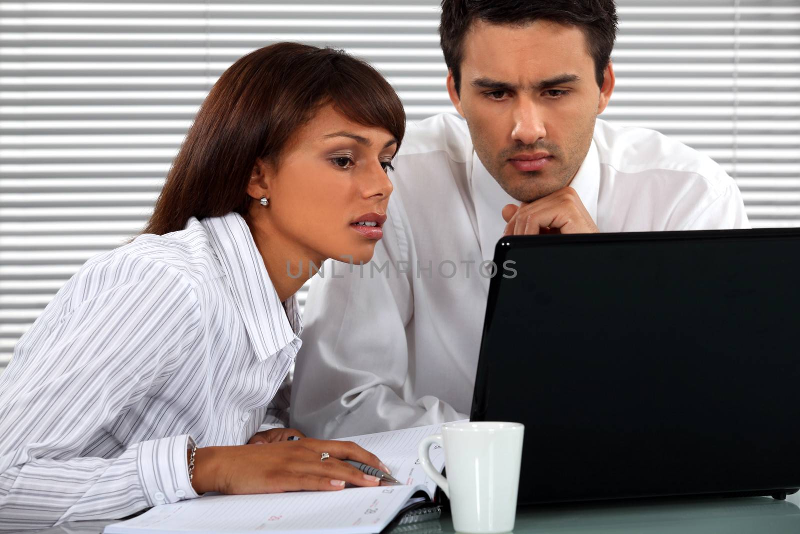 Business couple sitting at a laptop by phovoir