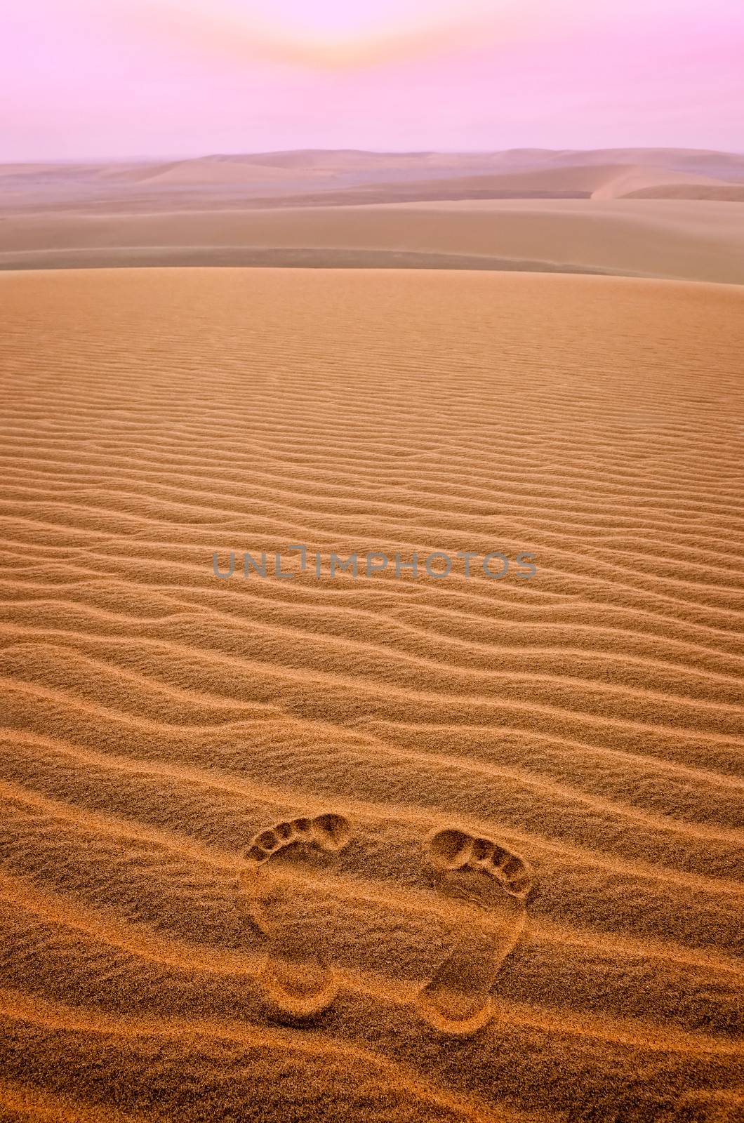 Two footprints in sand in the desert at sunset