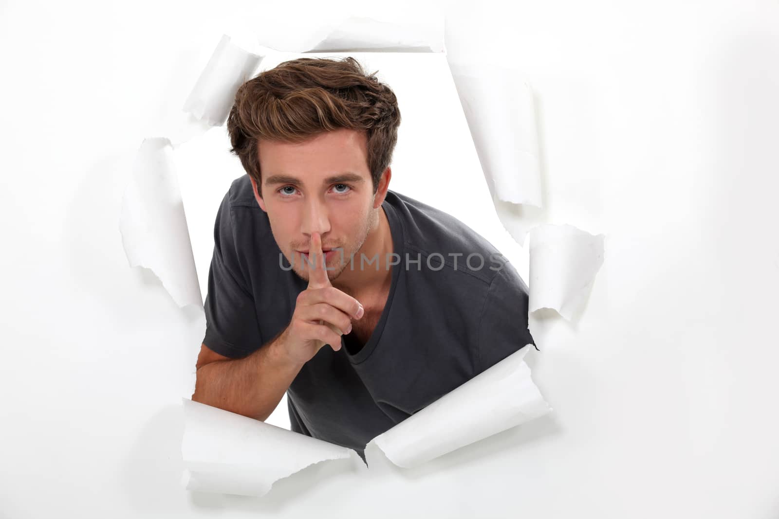 young man holds finger before his mouth by phovoir