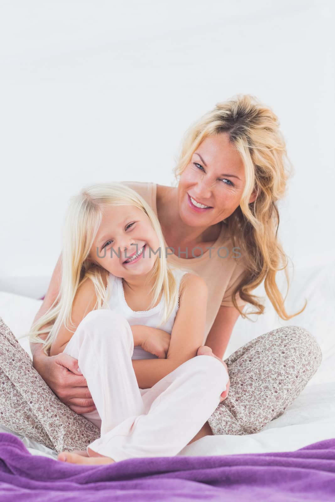 Mother and her daughter looking at camera sitting on bed