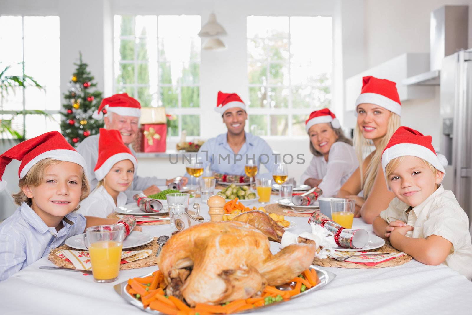 Happy family wearing santa hats around the dinner table at christmas