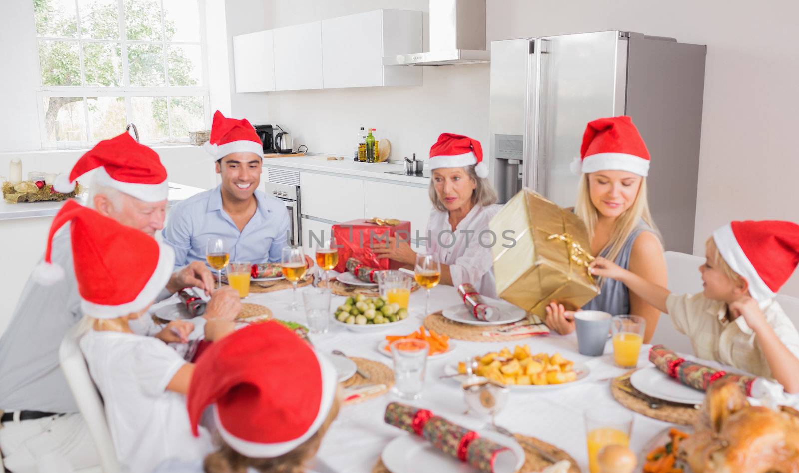 Smiling family at the dinner table at christmas exchanging gifts wearing santa hats
