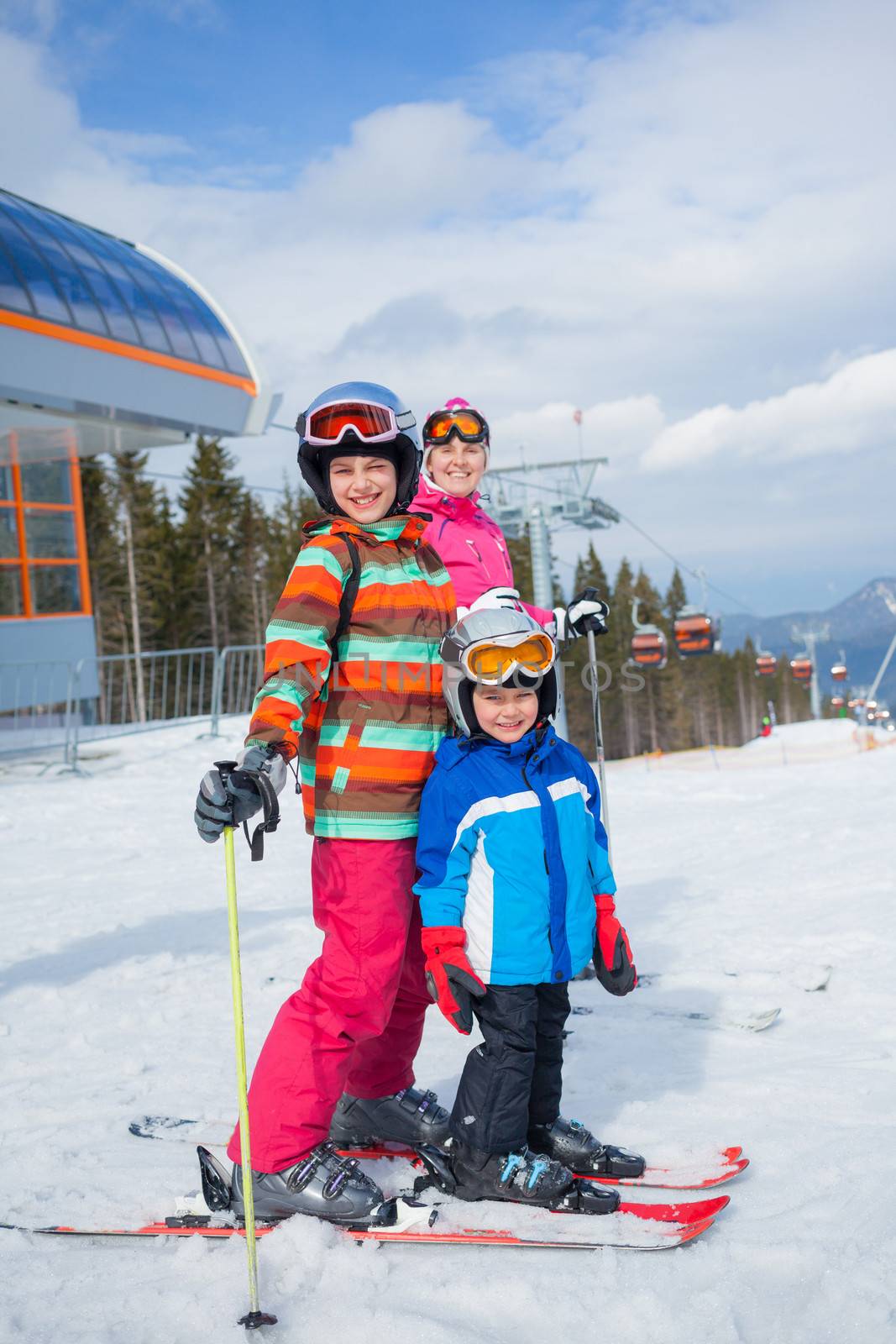 Two happy smiling kids in ski goggles and a helmet with his mother in the mountains
