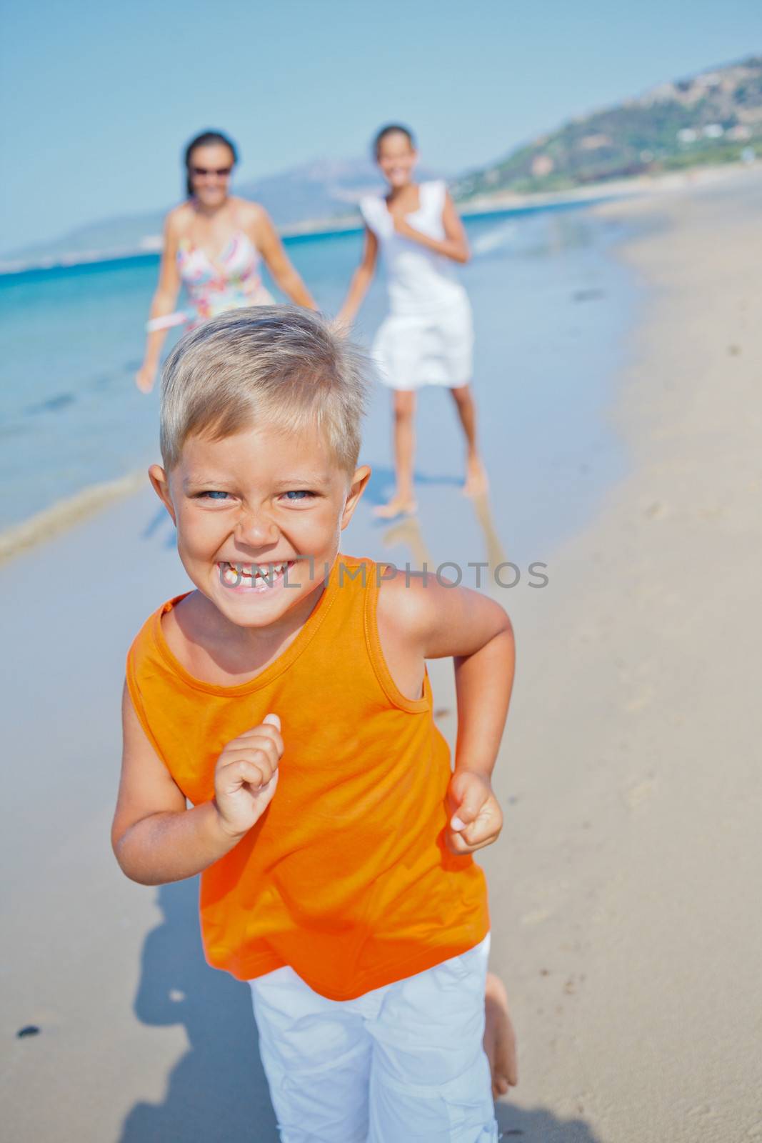 Adorable happy boy with sister and mother running on beach