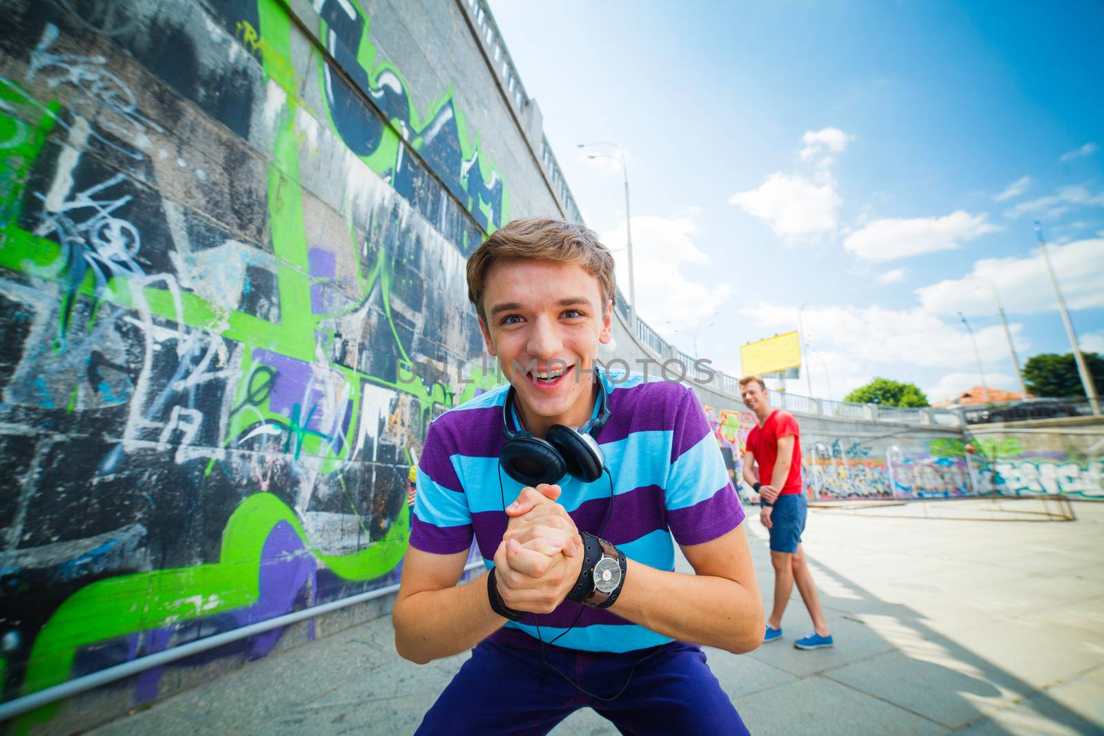 Portrait of happy teens boy with his friends by painted wall looking at camera
