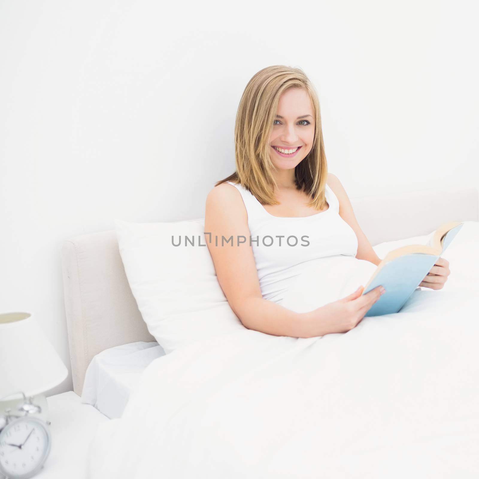 Portrait of happy young woman reading book in bed at home