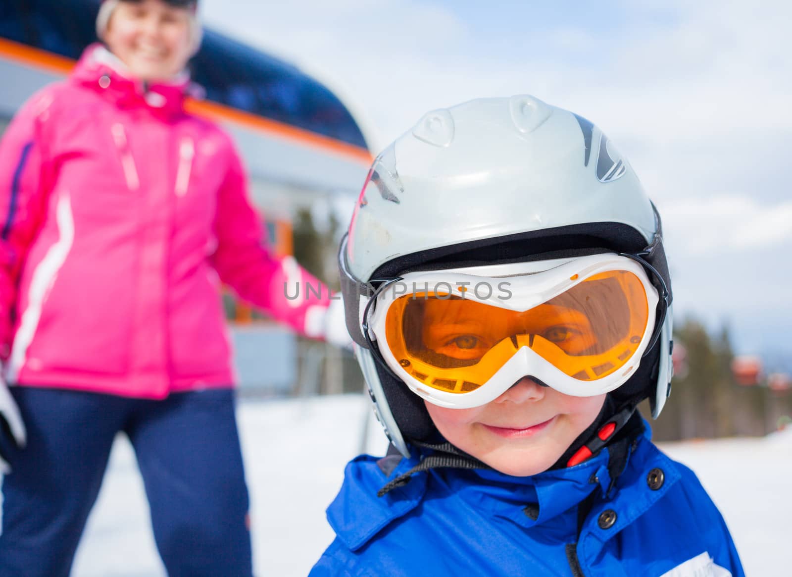 Portrait closeup of happy smiling boy in ski goggles and a helmet with his mother