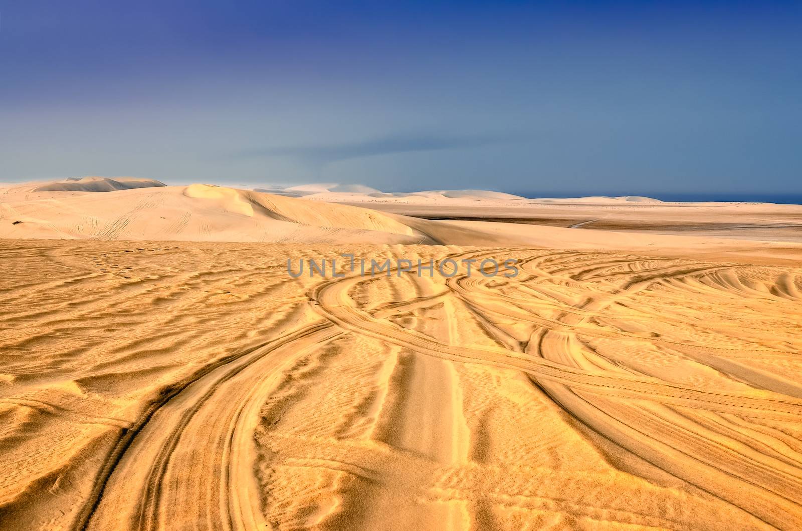 Detail of tyre tracks in sand desert with blue sky background