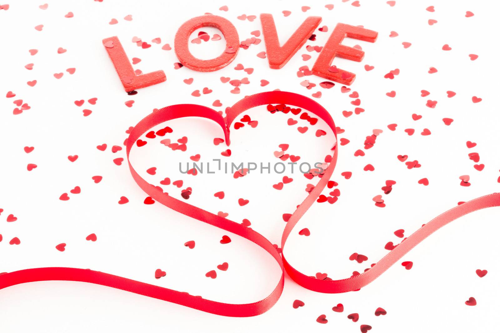Heart shaped ribbon with confetti and word love on white background