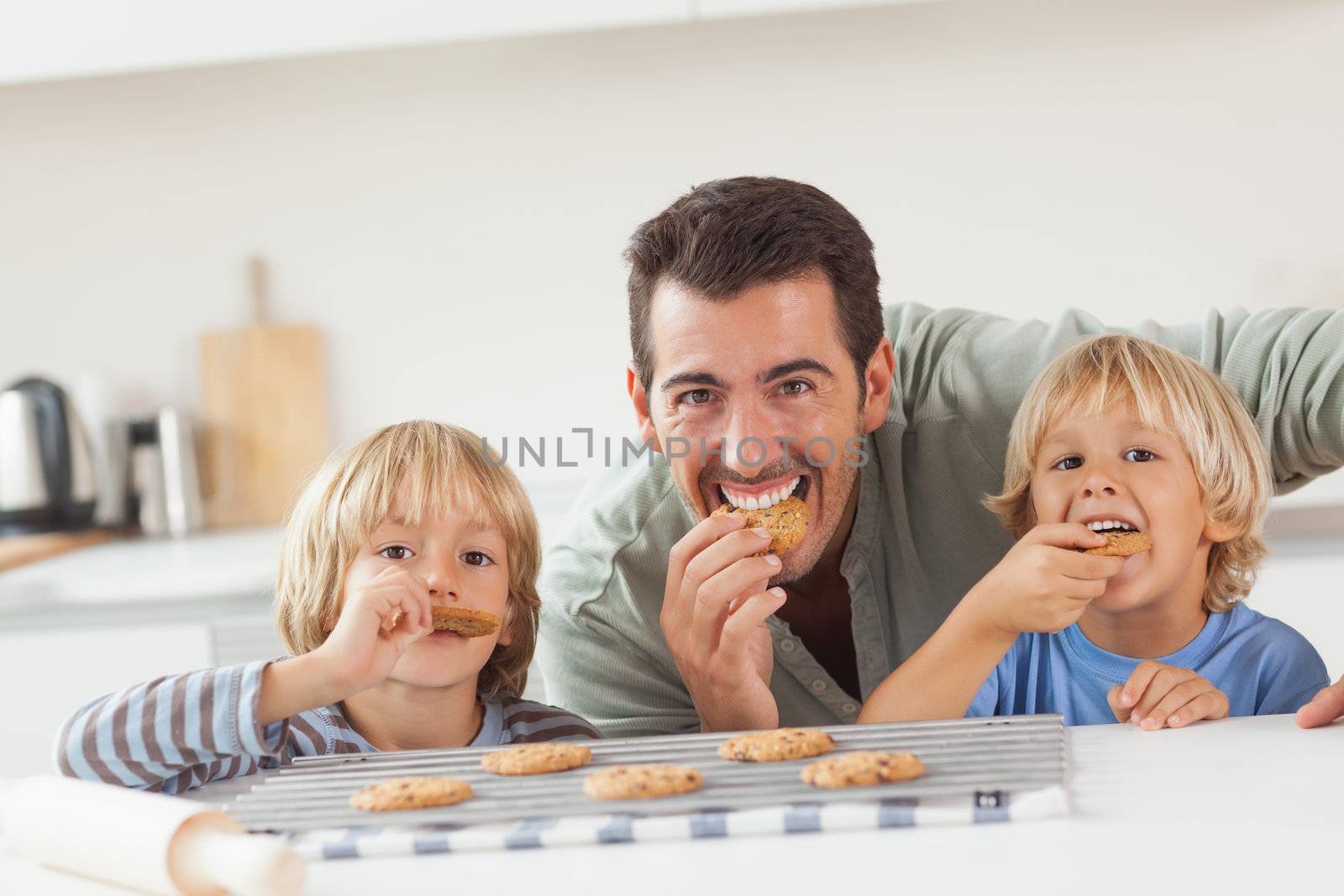 Smiling father and his sons eating cookies in the kitchen