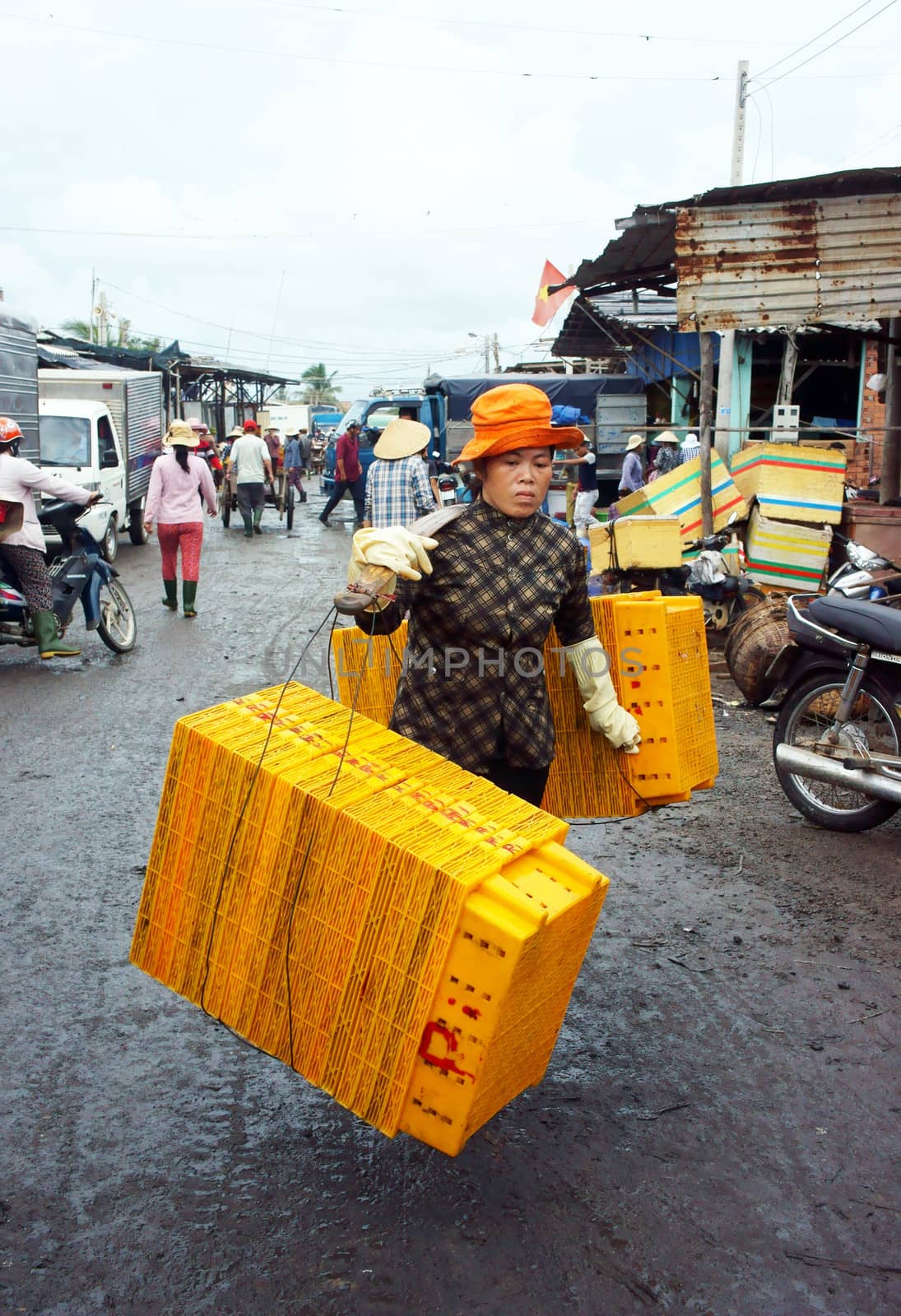 The women with tired face rattan plastic tray into market, she wear yellow hat, step on marshy. July 15, 2013