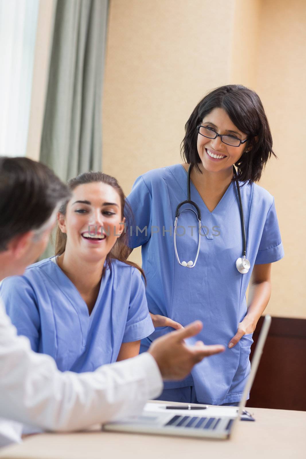 Nurses laughing with doctor using laptop in a meeting