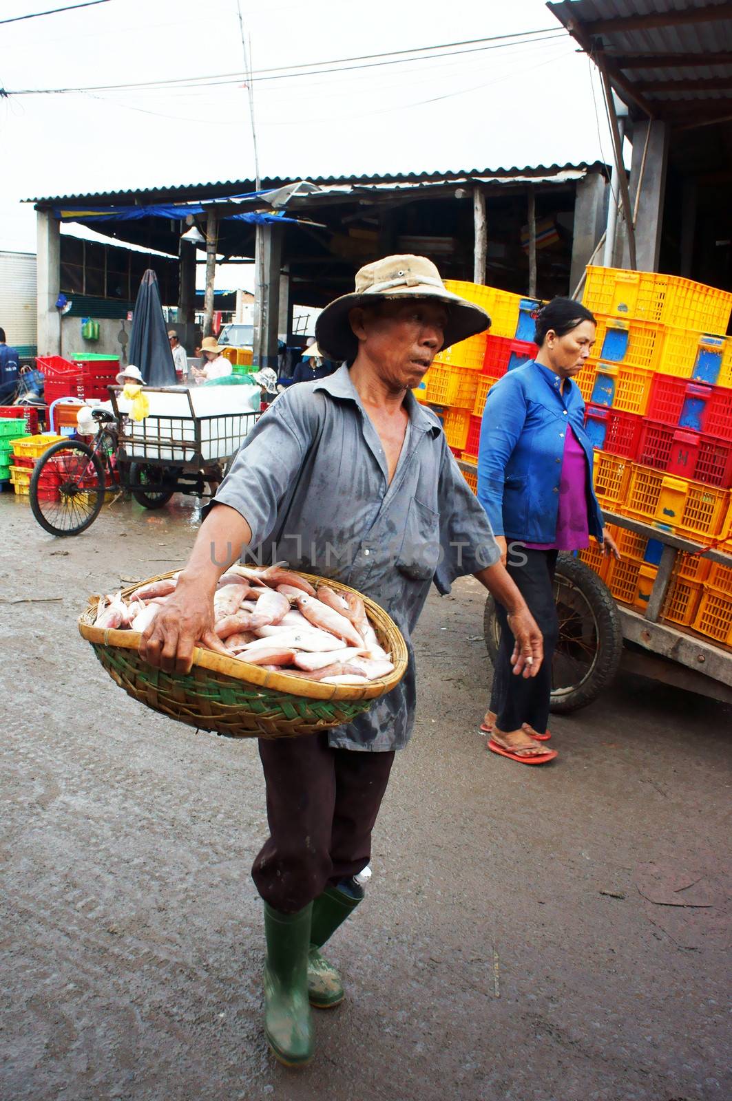 The man with tired face carry fish basket into fishing market in vertical frame. July 15, 2013