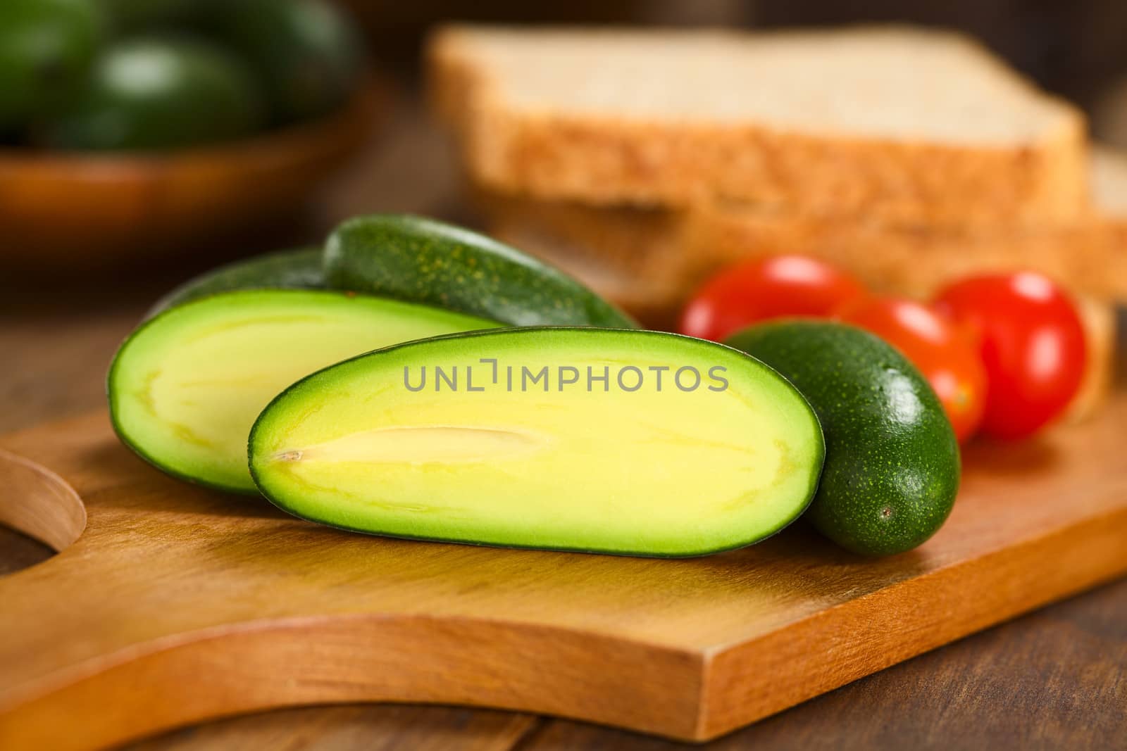 Half finger or cocktail avocado on wooden board with toast bread slices and cherry tomatoes in the back  (Selective Focus, Focus on the the upper part of the avocado half ) 