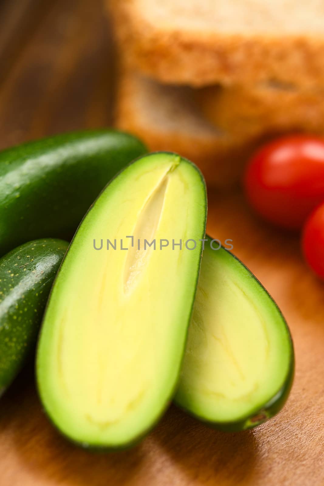 Half finger or cocktail avocado on wooden board with toast bread slices and cherry tomatoes in the back (Very Shallow Depth of Field, Focus in the middle of the image) 