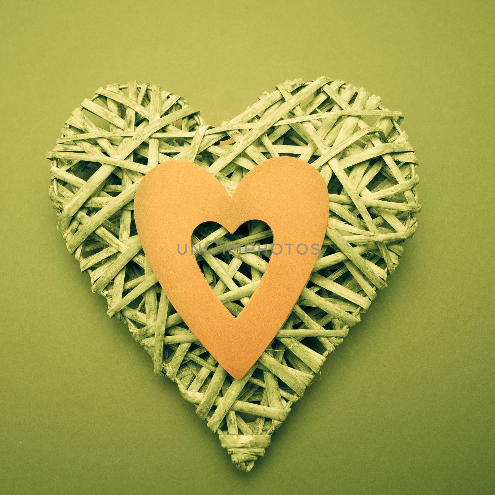 Wicker heart ornament with yellow paper cut out on green background