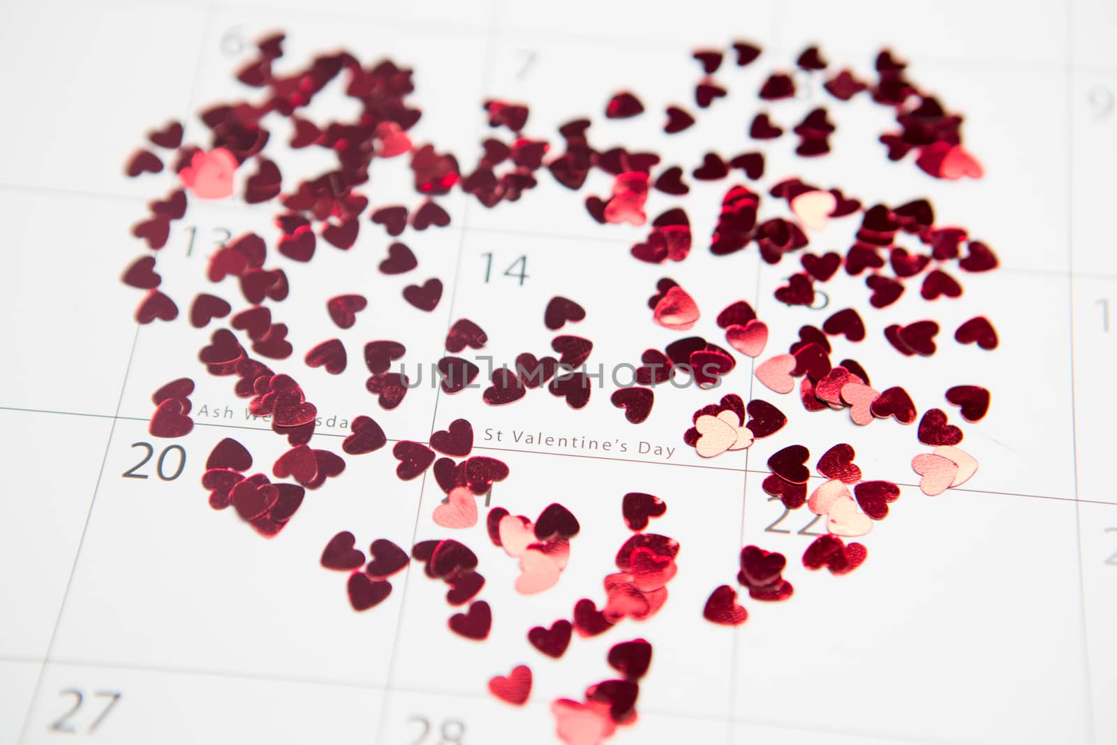 Pink confetti scattered in heart shape over valentines day on calendar