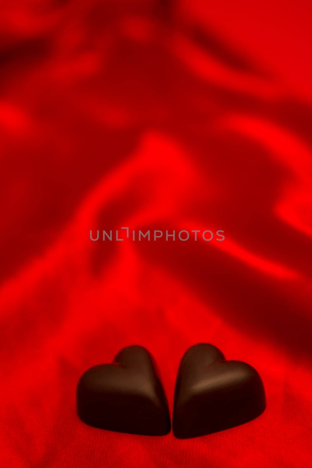 Two chocolate hearts on red silk background