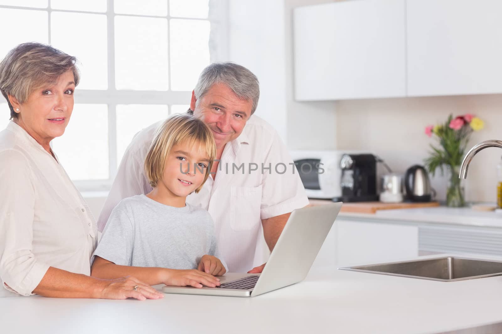 Child and grandparents looking at camera with a laptop in kitchen