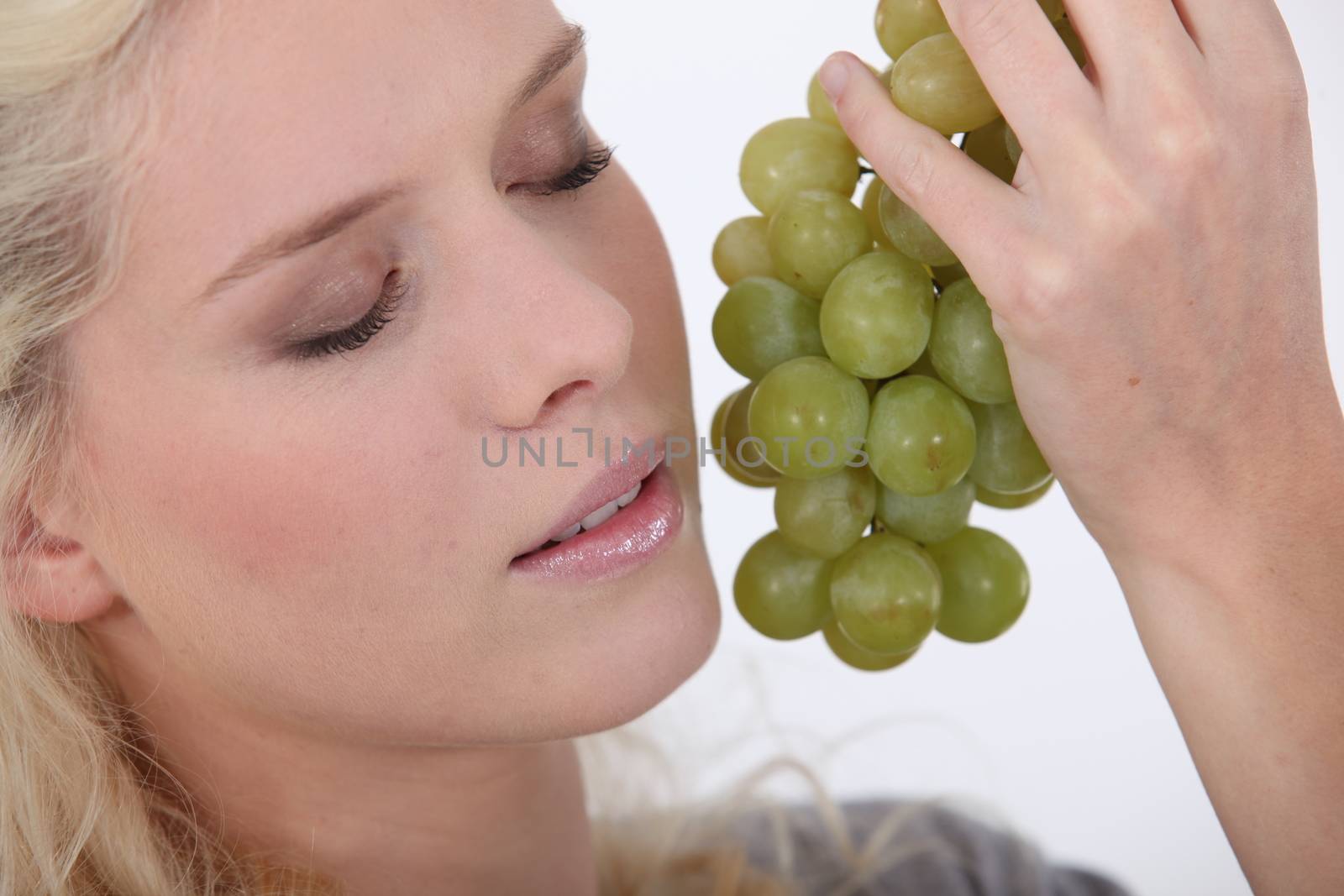 Woman holding a bunch of grapes next to her face by phovoir
