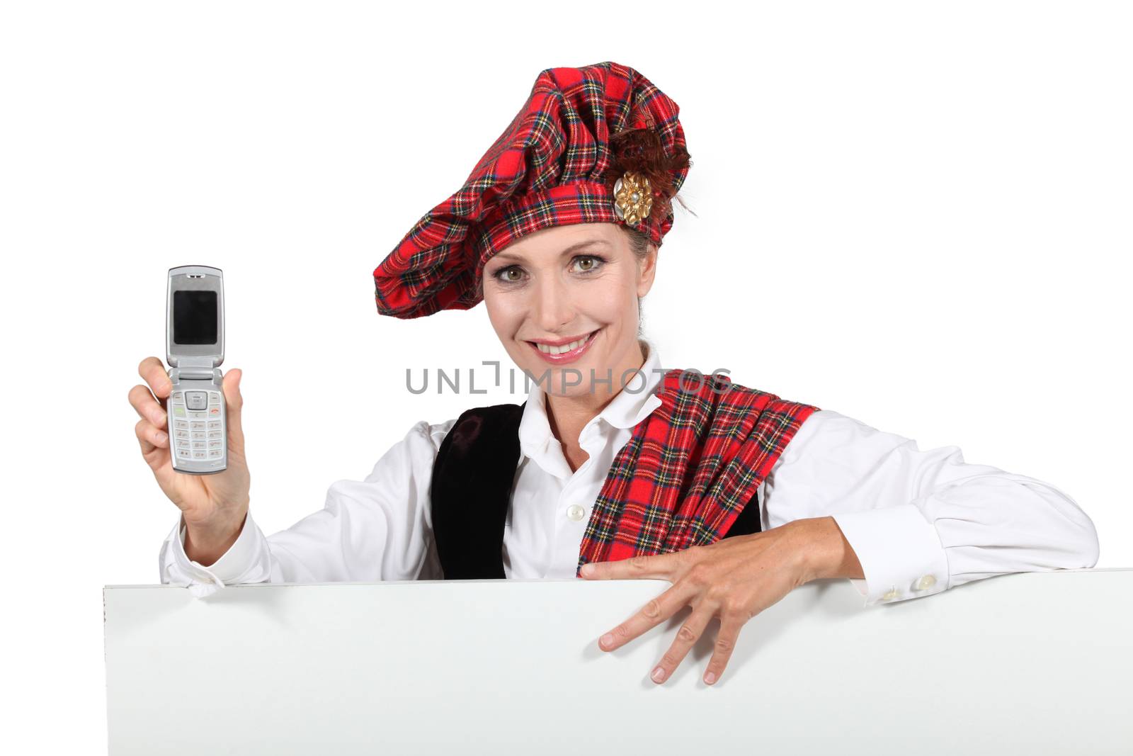 Woman in a Scottish outfit with a mobile phone and a board left blank for your message by phovoir
