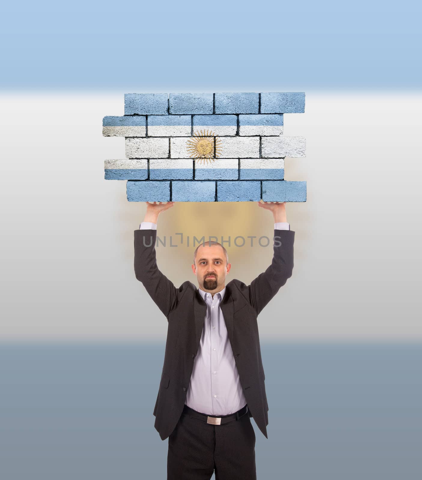 Businessman holding a large piece of a brick wall, flag of Argentina, isolated on national flag