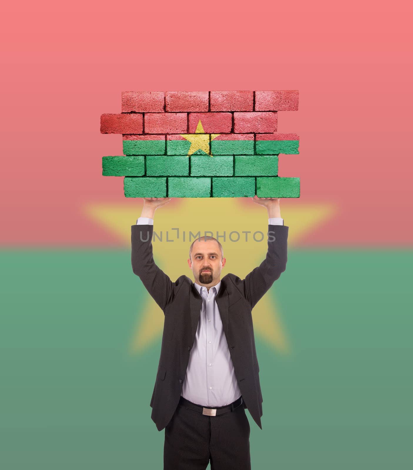 Businessman holding a large piece of a brick wall, flag of Burkina Faso, isolated on national flag