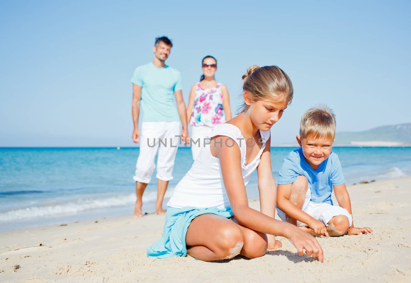 Family of four having fun on tropical beach - two cute kids playing with sand