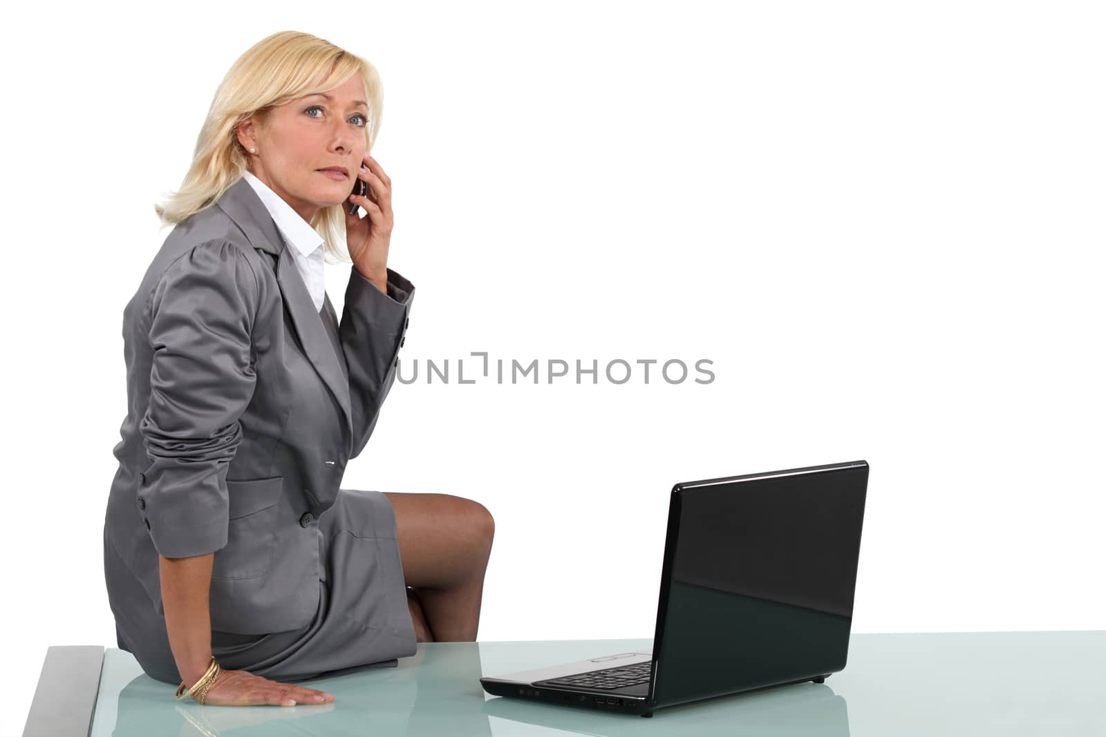 Senior businesswoman sitting on her desk by phovoir