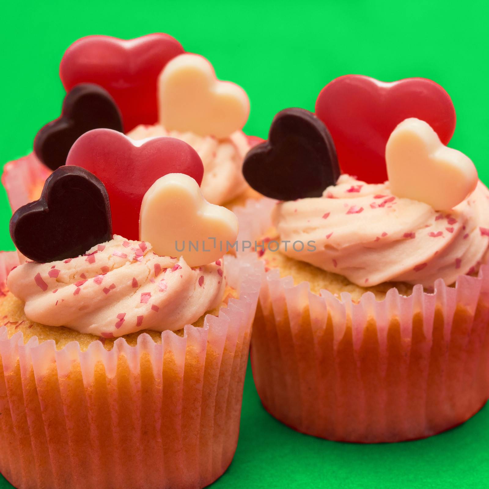 Close up of three valentines cupcakes on green background