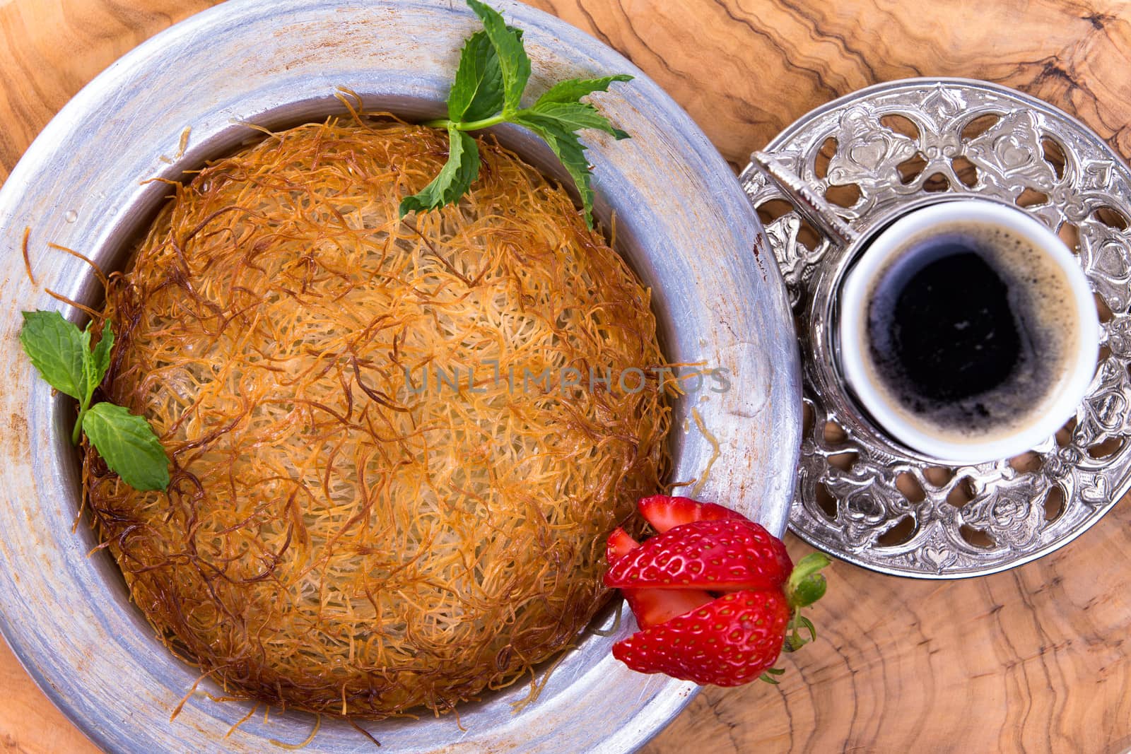 Turkish dessert kunefe isolated on a olive tree table with mints and sliced strawberry along with Turkish coffee