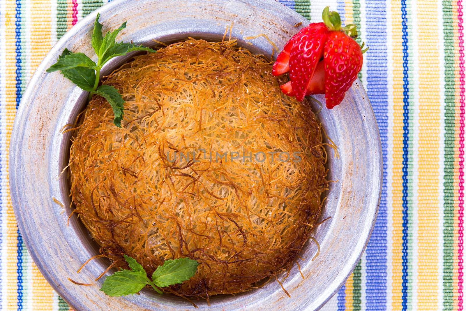 Turkish dessert kunefe isolated on a picnic cloth with mints and sliced strawberry