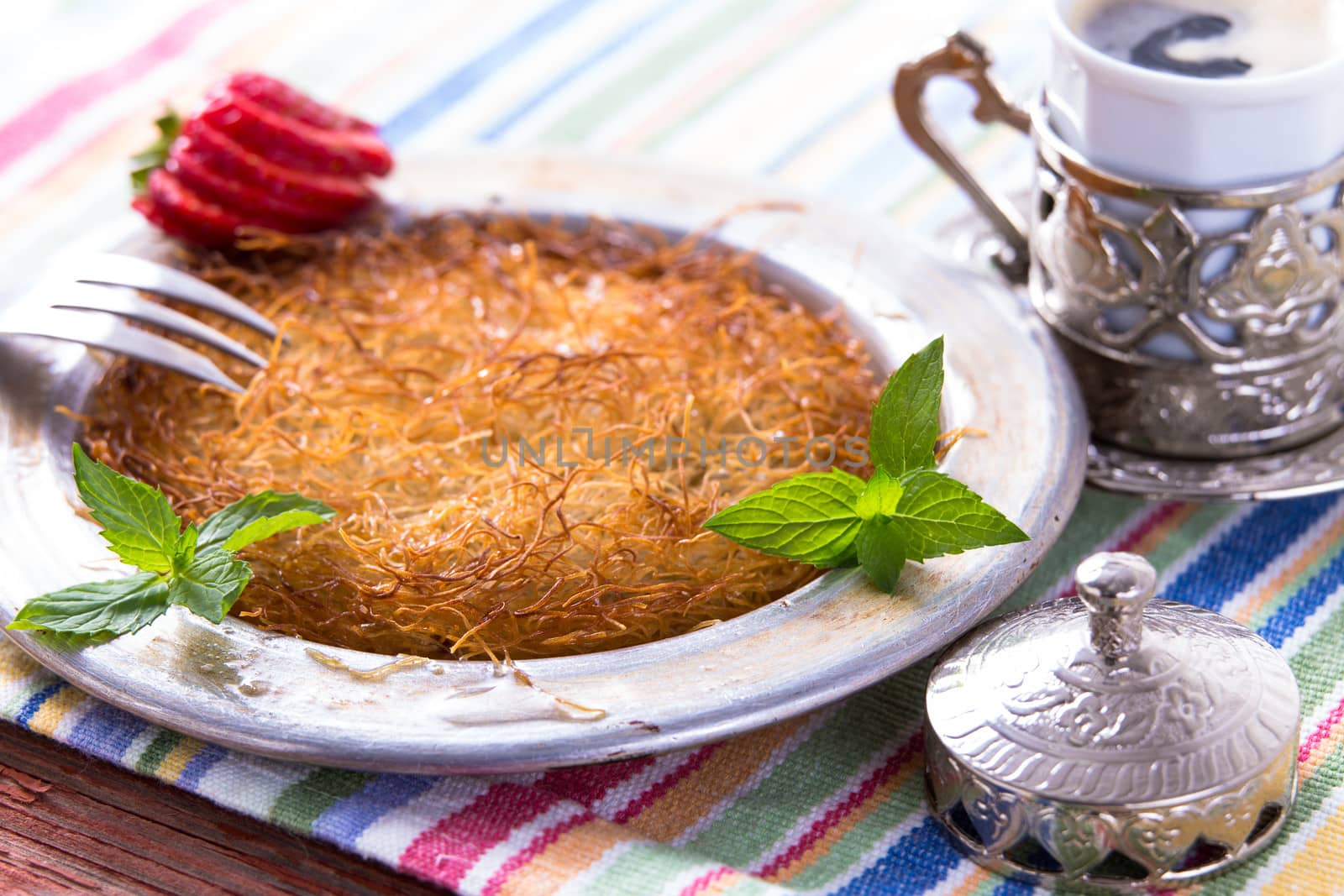 Turkish dessert kunefe  served in classical aluminum plate on a picnic table with mints and sliced strawberry along with Turkish cofffee