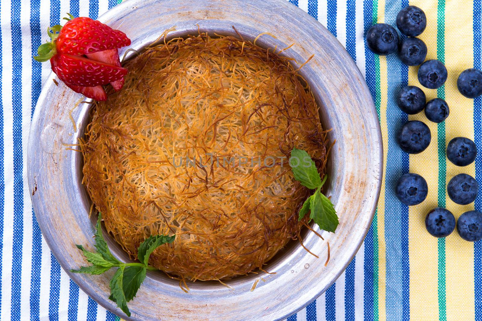 Turkish dessert kunefe on a picnic cloth with mints and sliced strawberry along with blueberries